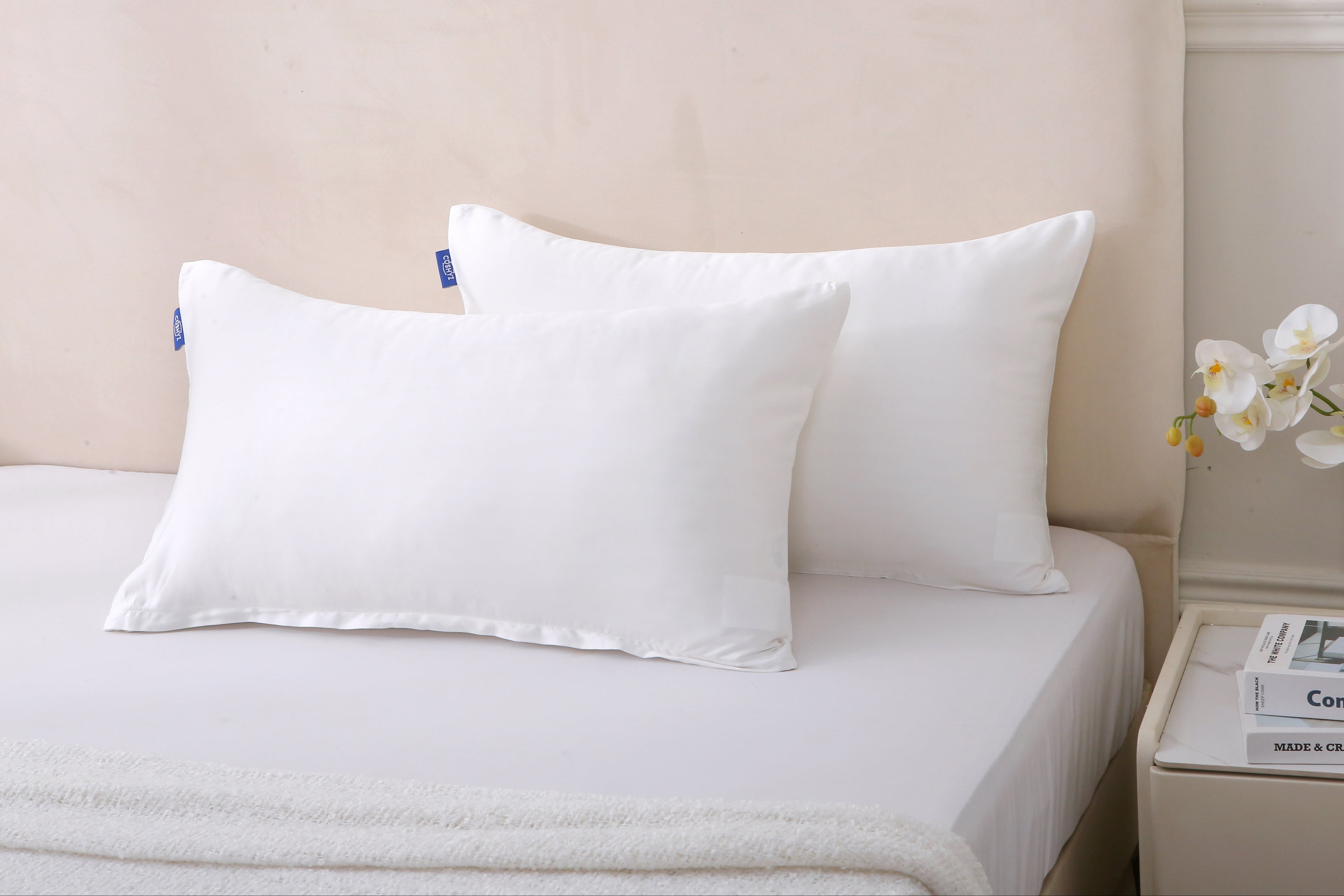Cushyz bamboo cooling white pillow covers on pillows placed on a neatly made bed with a neutral headboard and fresh flowers on the bedside table.